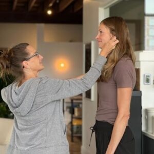 Two Women Practicing Muscle Testing with one woman placing her hand near the other woman's ear.